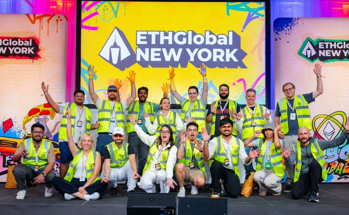 Group photo of the ETHGlobal New York hackathon team wearing yellow safety vests, posing on stage in front of the ETHGlobal New York branded backdrop.