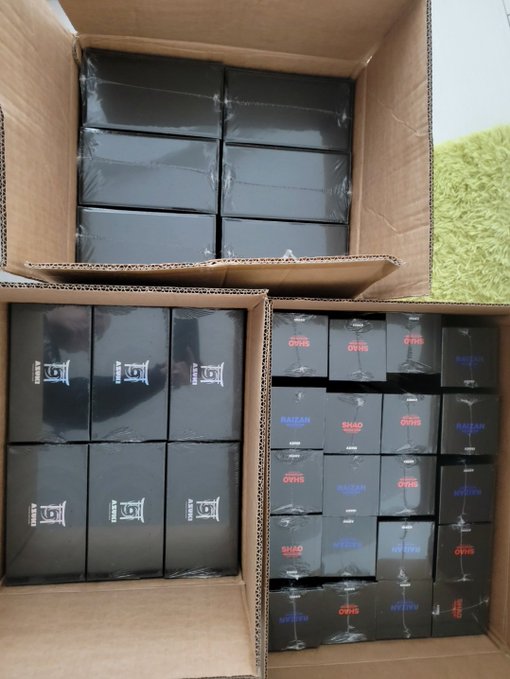 Cardboard boxes filled with shrink-wrapped black product boxes labeled 'SILK LOUIS' and 'BAZAAR' are stacked on a green carpeted floor.