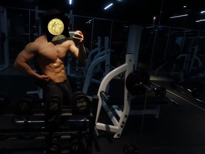 A shirtless, muscular man takes a mirror selfie in a dimly lit gym, with dumbbells (one labeled "5.7FT") and weight equipment visible around him, while holding a phone that obscures his face. The image contrasts the post's lament about gaining body fat and disrupted sleep from going full-time into web3, highlighting the physique he worries about losing.