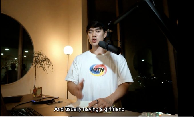 A young man wearing a white "Kith" t-shirt speaks into a microphone in a dimly lit room, with subtitles reading "And usually having a girlfriend." The image appears to be from a podcast or YouTube video where the host is discussing relationships, which aligns with the post's frustration about a trading influencer suggesting that having a girlfriend is necessary to become a better trader.