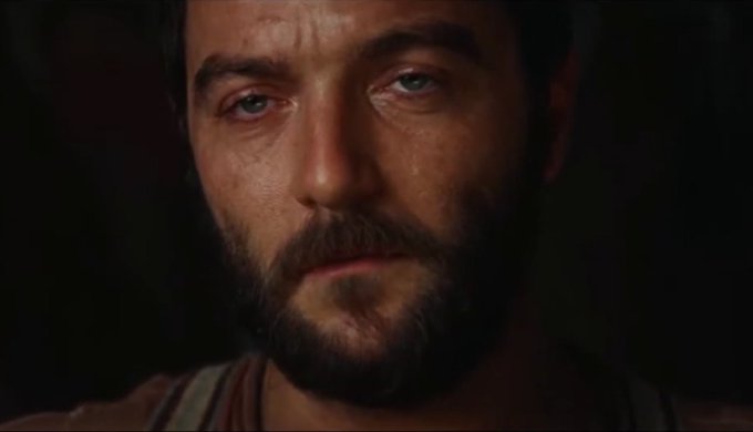 A close-up shot of a man's face with a beard, appearing tearful and emotional, likely from a video game or film cinematic.