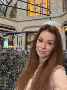 A woman with long brown hair smiles in a beautiful, light-filled café or atrium. The peaceful morning coffee setting complements the post’s feeling that “green candles” and coffee are the best therapy, and that she has “Always loved green.”