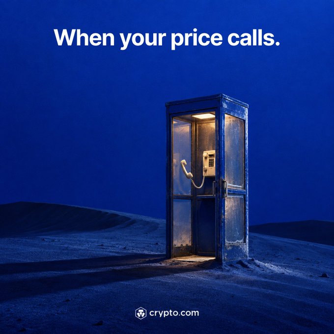 A glowing phone booth stands isolated in a dark, blue-toned desert landscape with the headline "When your price calls." at the top and the crypto.com logo at the bottom. The imagery visually reinforces the post's message by symbolizing a "call" to alert crypto users, much like a ringing telephone, encouraging them to set price alerts in the Crypto.com App so they don't miss important market moves.