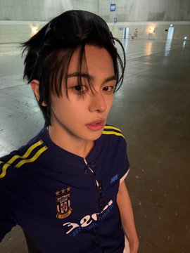 A young woman with dark, tousled hair poses indoors wearing a blue and yellow athletic jersey featuring "IZOD" text and a team crest. The image accompanies hashtags referencing "ALPHADRIVEONE," "ALD1," "알파드라이브원," and "LEO/리오," suggesting she may be a member of the Alpha Drive One K-pop group, specifically associated with the member Leo.