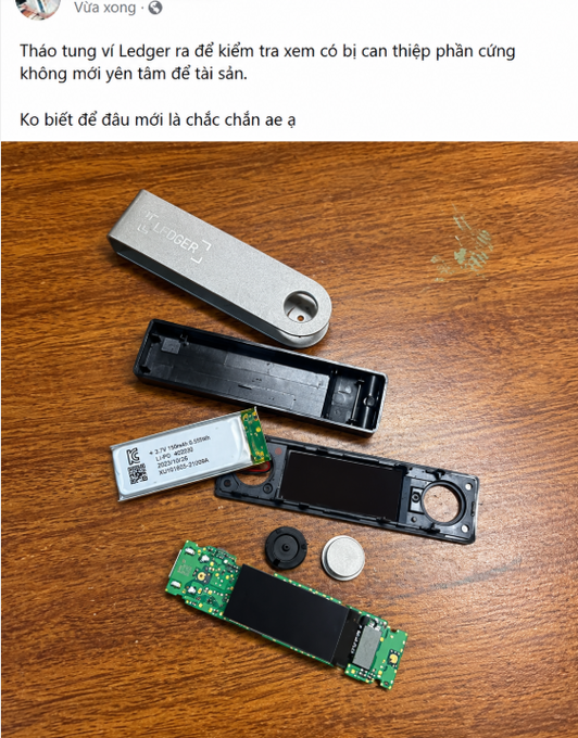 A disassembled Ledger hardware wallet, with its metal casing, internal circuit board, and battery components spread out on a wooden surface, showing the device has been taken apart to inspect for tampering.