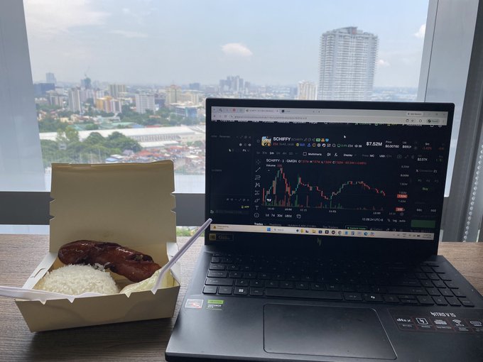 A laptop on a wooden desk displays a crypto trading chart for "SCRIFFY" at $7.52M, with a takeout box of rice and sausage beside it, overlooking a cityscape from a high-rise window.
