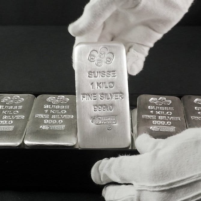 Gloved hands hold up a 1-kilo PAMP Suisse "SUISSE 1 KILO FINE SILVER 999.0" bar, with identical bars lined up behind it, visually emphasizing the silver component of the "Gold Silver XRP" investment theme.