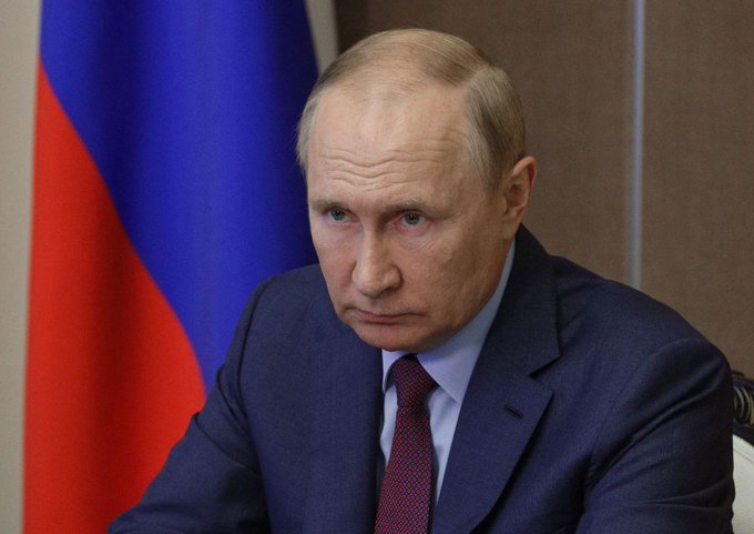 Vladimir Putin sits before the Russian flag in this image, illustrating the subject of the post regarding Russia's new regulatory laws for cryptocurrency.