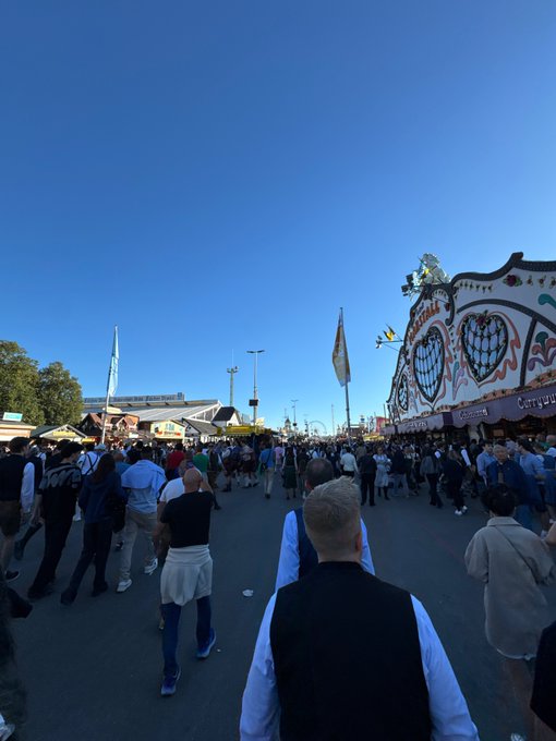 A bustling crowd walks through what appears to be Oktoberfest in Munich, with traditional Bavarian festival tents visible, including signs for "Café-..." booths, under a clear blue sky — capturing the lively atmosphere that supports the claim that "Bavaria is the best country in the world."