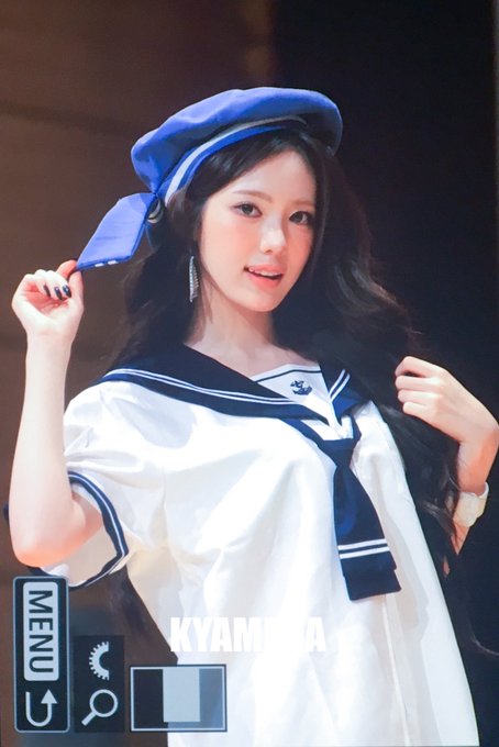 A young woman with long dark hair wearing a sailor-style outfit with a blue beret, posing with one hand near her face.