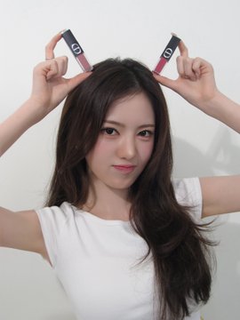 A young woman with long dark hair wearing a white t-shirt poses playfully with two dark, rectangular objects held above her head against a plain white background.