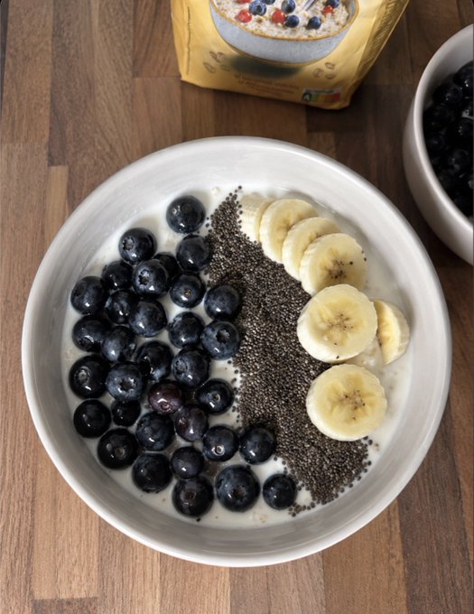 The image shows a bowl of cereal with blueberries, bananas, and chia seeds. There are also two bowls containing more blueberries nearby. The scene appears to be set up for a meal or snack, possibly during breakfast time.