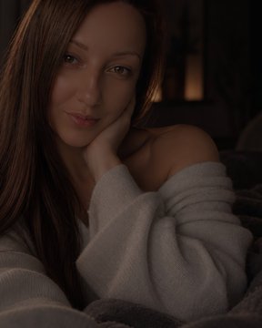 A dimly lit portrait of a woman with long brown hair resting her face on her hand, wearing an off-the-shoulder sweater.