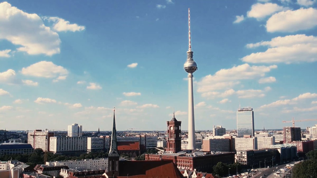 The image shows a cityscape with a tall white tower dominating the skyline. The tower has a spire at its peak, which adds to the overall grandeur of the scene. In the foreground, there are buildings that contribute to the urban atmosphere. The photo is taken from an elevated perspective, providing a comprehensive view of the city's layout and architectural features.