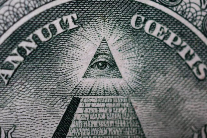 A close-up macro photograph of the reverse side of a US one-dollar bill, prominently showing the 'ANNUIT COEPTIS' text and the Eye of Providence within a pyramid.