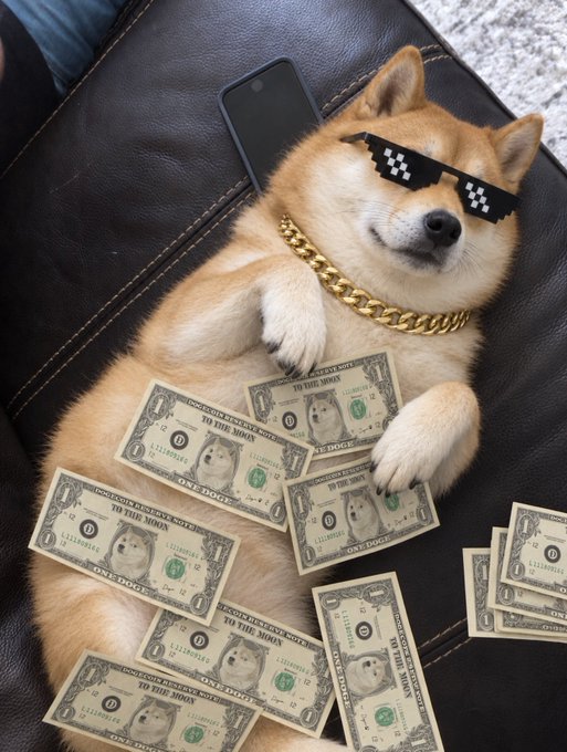 A Shiba Inu wearing pixelated "deal with it" sunglasses and a gold chain lounges on a leather couch surrounded by "Doge" dollar bills and a smartphone. The image playfully visualizes the post's message about Dogecoin being money, with the dog literally "making it rain" with Doge-themed currency.