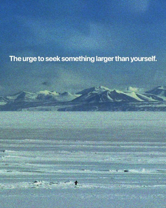 A vast snowy landscape with distant mountains and a tiny figure walking across the ice, with the text overlay 'The urge to seek something larger than yourself.'