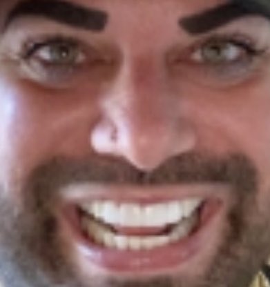A close-up of a grinning man with a thick beard, mustache, and prominent dark eyebrows, presented as a mysterious "dream figure" appearing to members of the Blockchain Twitter community. The exaggerated, almost surreal facial expression and tight framing give the image an unsettling, dreamlike quality fitting its role as a viral internet apparition.