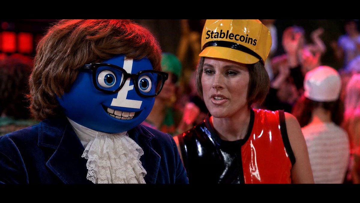 The image features a woman wearing a yellow hard hat, standing next to a blue character with glasses that has a face painted on its head. The woman appears to be dressed as a character from the movie "Stablecoins", while the blue character is wearing a suit and tie. Both characters are in front of a crowd of people who seem to be watching them intently.