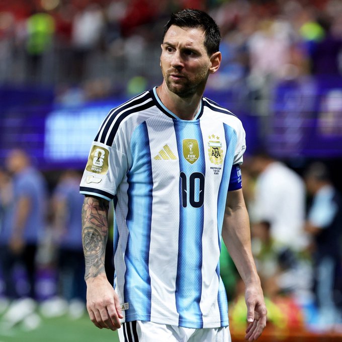 Lionel Messi wearing the Argentina national team jersey with number 10, standing on the pitch during what appears to be a match, with a FIFA World Cup 2022 patch visible on the sleeve.