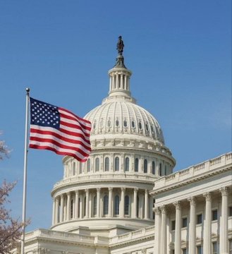 The U.S. Capitol dome stands beneath a clear blue sky with the American flag waving in the foreground, symbolizing the legislative process behind the upcoming revised CLARITY Act aimed at establishing U.S. crypto market structure. The image represents the congressional deliberations referenced in the post, where lawmakers are working to finalize the bill pending an ethics agreement.