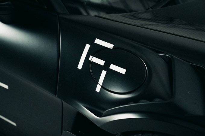 A close-up of a sleek black motorcycle fuel tank displays a stylized white "FT" logo, aligning with the teaser "The frontier is opening soon" by hinting at an upcoming new bike or brand model. The minimalist design and dark finish evoke a sense of premium performance and anticipation.
