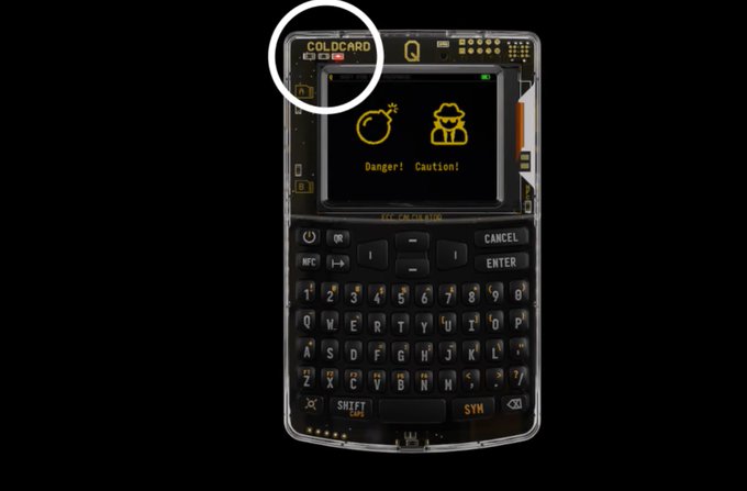 A handheld electronic device labeled 'GOLDCARD' with a QWERTY keyboard and screen displaying 'Danger! Caution!' alongside icons of a bomb and a thief.