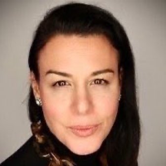 A portrait photo of a woman with long dark hair pulled back, wearing a dark top against a plain gray background.