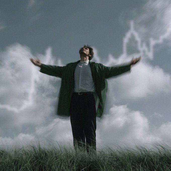 A young man in a green jacket and white shirt stands with arms outstretched and head tilted back in a field of tall grass, against a dramatic cloudy sky with a faint castle outline visible in the clouds.

**How it relates to the post:** The image's serene, open-armed pose and dreamy sky evoke a sense of freedom and effortless ease—mirroring the post's message of smooth, uninterrupted 24/7 trading on OKX, as if the user is welcoming the Friday morning with a carefree, fluid experience.