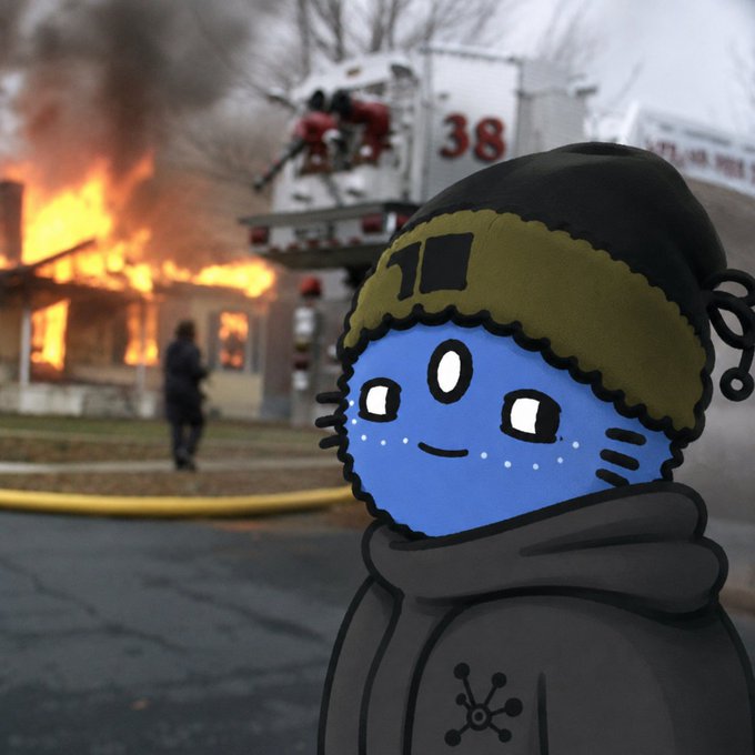 A blue cartoon character in a black hoodie smiles in front of a burning building, while firefighters from truck "38" battle the flames in the background. The image creates an ironic contrast to the cheerful "gm, happy weekend" greeting, humorously highlighting that someone is clearly not "winning" today.
