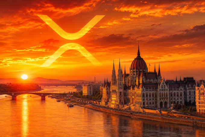A dramatic sunset photograph of Budapest's Parliament building along the Danube River, featuring a large XRP cryptocurrency logo overlaid on the orange and red sky.
