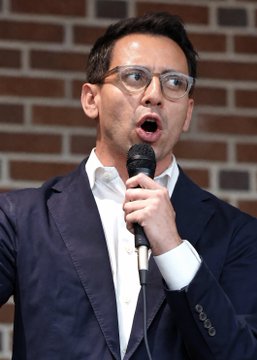 A man wearing glasses and a dark suit speaks passionately into a microphone against a brick wall background, likely at a political event. The image appears to depict Byron Donalds, the candidate mentioned as surging in the Florida GOP primary according to the accompanying post.