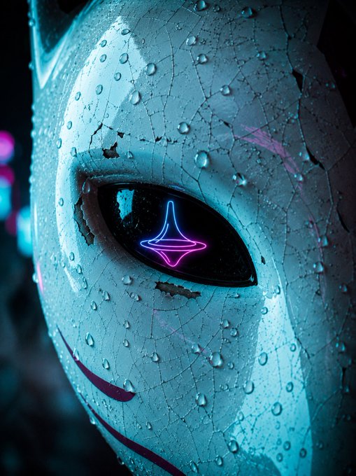 Close-up of a cracked, weathered cyan-colored mask or face with a glowing pink and blue neon diamond/star shape in its dark eye socket.