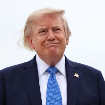 Former President Donald Trump, wearing a navy suit with a blue tie and an American flag lapel pin, smiles slightly while looking off-camera. The image accompanies a post about his recent comments suggesting inflation could rapidly reduce the U.S. national debt, a claim tied to broader discussion of potential economic ripple effects.