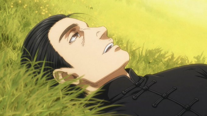 An anime character with dark hair and blue eyes lies on his back in tall green grass, gazing upward with a faint smile.