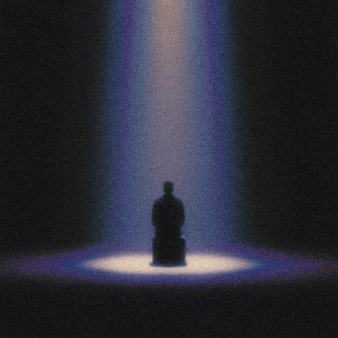 A silhouette of a person sitting on a chair or block in a dark, grainy void, illuminated from above by a single spotlight that casts a soft purple and white glow.