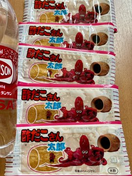 A photo showing several packages of Japanese snacks labeled '明太子せん太郎' (Mentaiko Senbero) stacked on a table, with a bottle of 'TASCO' sauce partially visible on the left.