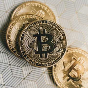 The image features a group of five gold Bitcoins, all of which have different designs, sitting next to each other on top of a white background. The largest Bitcoin appears at the bottom left corner while two more smaller ones are placed towards the right side of the frame. Below this scene, there is text that reads "BULLISH: $700 billion Visa says Bitcoin & crypto will boom like e-commerce did in the 19900s."