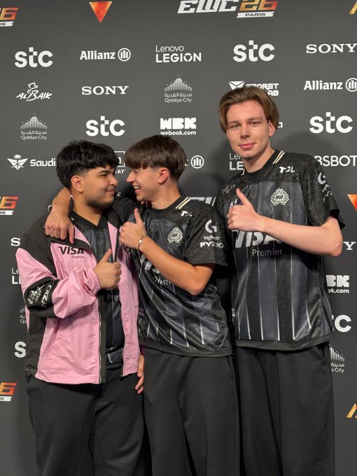 Three teammates pose together with thumbs up at the EWC 2026 Paris event, with one wearing a pink jacket and the other two in black "VIP" jerseys, all smiling in front of a sponsor backdrop featuring Allianz, Lenovo Legion, Sony, and stc logos, celebrating their qualification for the upcoming competition.