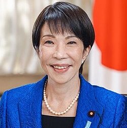 The image shows Japanese politician, Ryū Shionoya, who may be involved in the country's decision to eliminate tax regulations hindering yen stablecoin transactions. The Japanese flag is visible in the background.