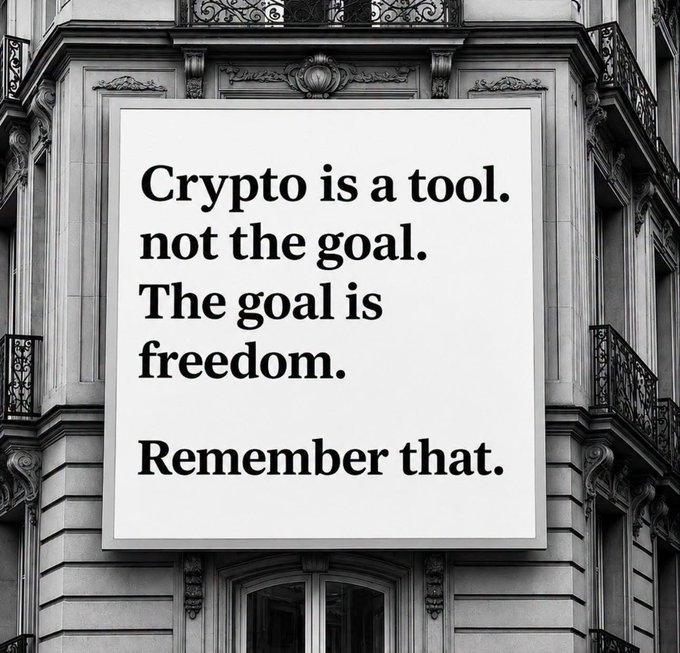 A black and white photograph of an ornate building facade with a large white sign in the foreground that reads: 'Crypto is a tool, not the goal. The goal is freedom. Remember that.'