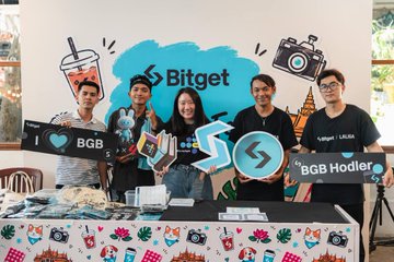 A cheerful group of five people pose together at a Bitget-branded event booth, with signage displaying "Bitget," "BGB," and "BGB Hodler," accompanied by props like a coffee cup and camera, reflecting the warm coffee meetup vibe mentioned in the post's #BitgetSipSip and #EventwithBitget hashtags with the BitgetSEA crew.