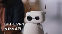 A small white humanoid robot with large black eyes stands on a table while overlaid text reads 'GPT-Live-1 in the API'.