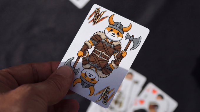 The image features a person holding up a playing card with a cartoon character on it that has an axe and a Viking outfit. The card also includes a message about financial responsibility, stating "No matter how hard financial situation gets, I have $FLOKI card under my sleeve". This playful combination of the card's design and the accompanying message creates a lighthearted atmosphere while still conveying an important message to the viewer.