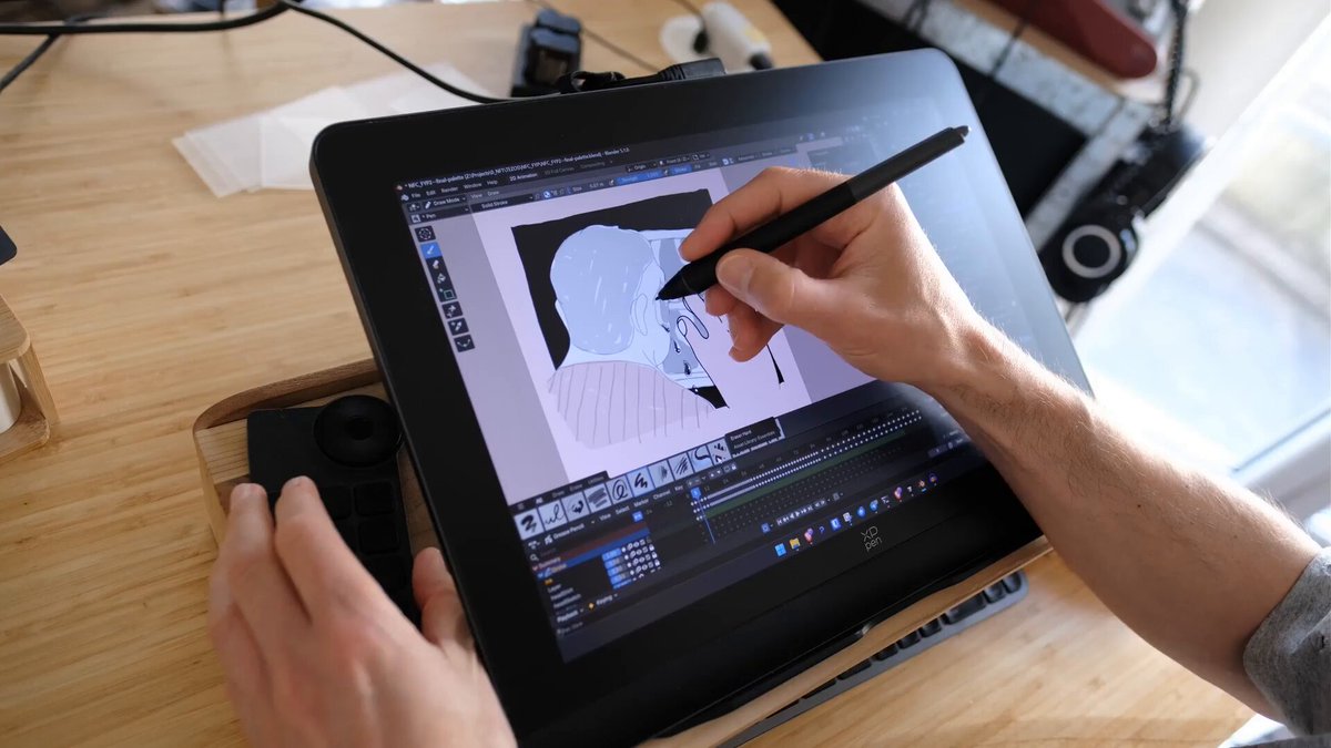The image shows a person using a tablet computer with a stylus, drawing or painting something on the screen. The tablet appears to be an iPad Pro, which has a stylus attached for more precise control while creating digital artworks. The person is sitting at a desk and seems to be engaged in their creative process.