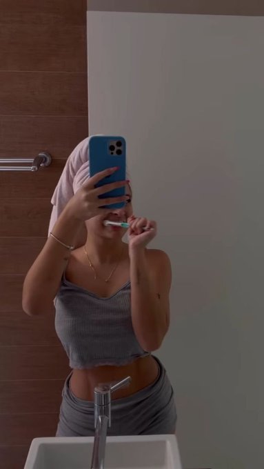A person takes a mirror selfie while brushing their teeth, wearing a gray two-piece outfit and a towel wrapped around their head. The image loosely connects to the post's theme of self-care routines and mindfulness practices linked to the TimeSoul ecosystem.