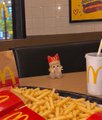 A McDonald's Happy Meal toy, appearing to be a small white cat figurine, sitting among french fries next to a drink cup.
