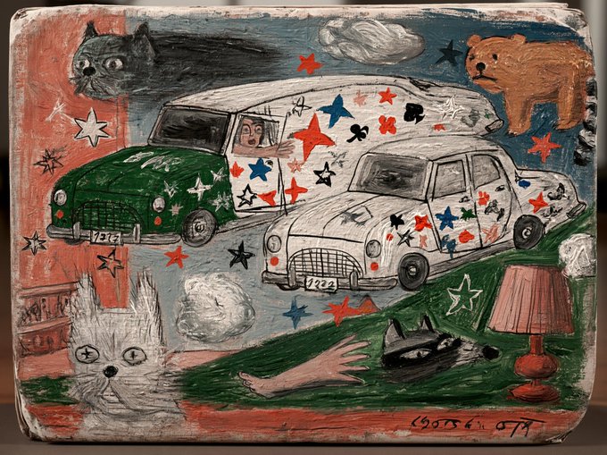 A naive-style painting depicting two cars, a white cat with a cross, a bear, and scattered playing card suits in red, blue, and black, with a signature dated '95' in the corner.