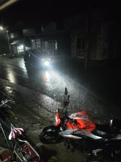 The image shows a motorcycle parked next to another motorcycle at night with rain falling around them, creating a moody atmosphere. The motorcycles are positioned close together, suggesting that they belong to the same owner or riders who may be spending time together on this rainy night. The photo also includes text elements such as "Good night, X family." and "@quipnetwork Super bullish @useTria". These elements add context to the scene and provide a sense of connection between the motorcycle owners and their shared interest in motorcycling.