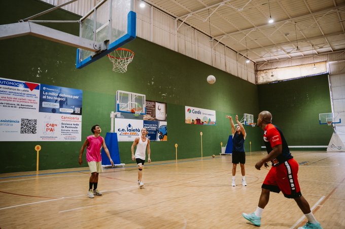 A group of people playing basketball in an indoor court with Spanish-language banners and posters on the walls.